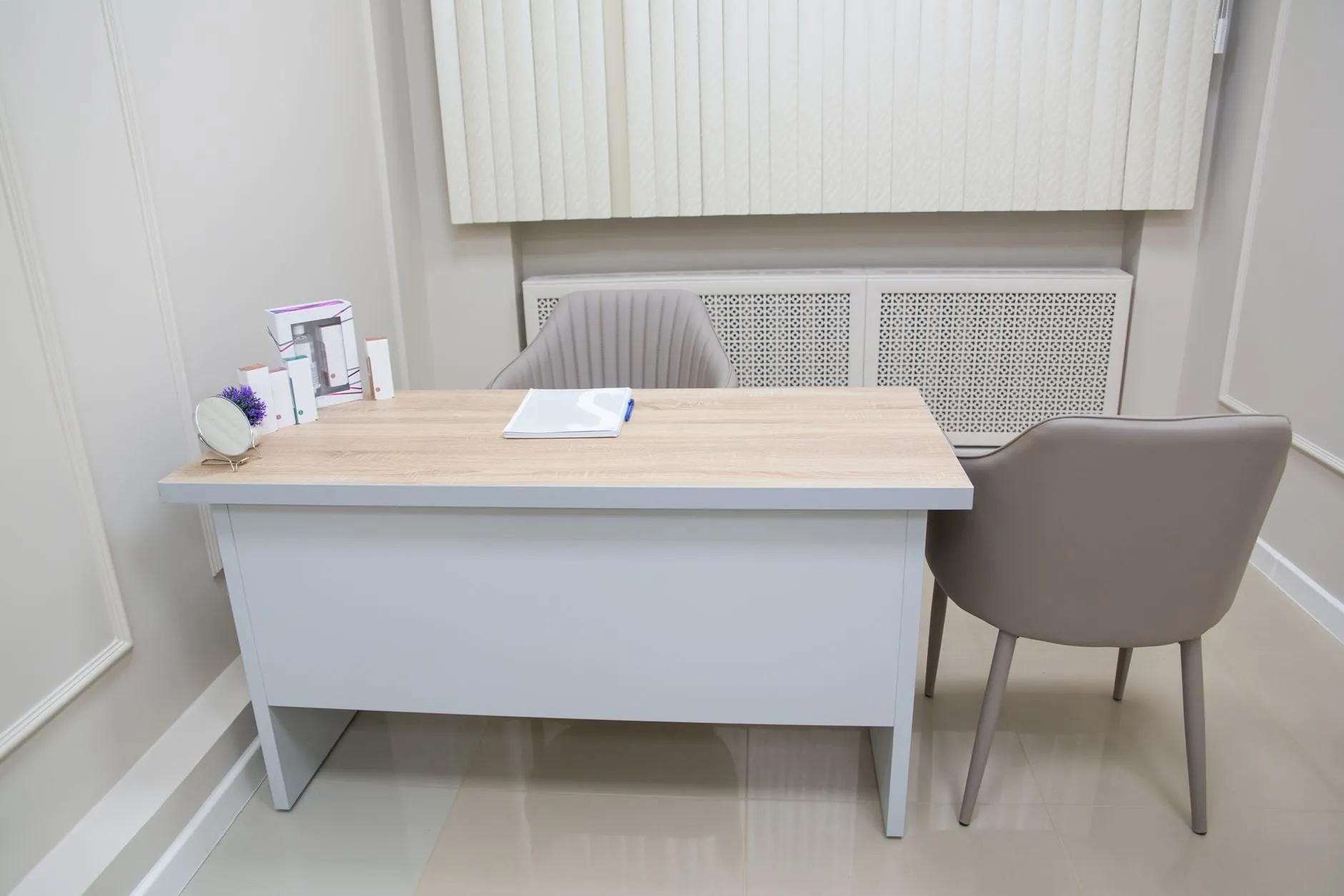 A tidy consulting room with a light oak desk, two upholstered chairs and a notepad ready for the next patient