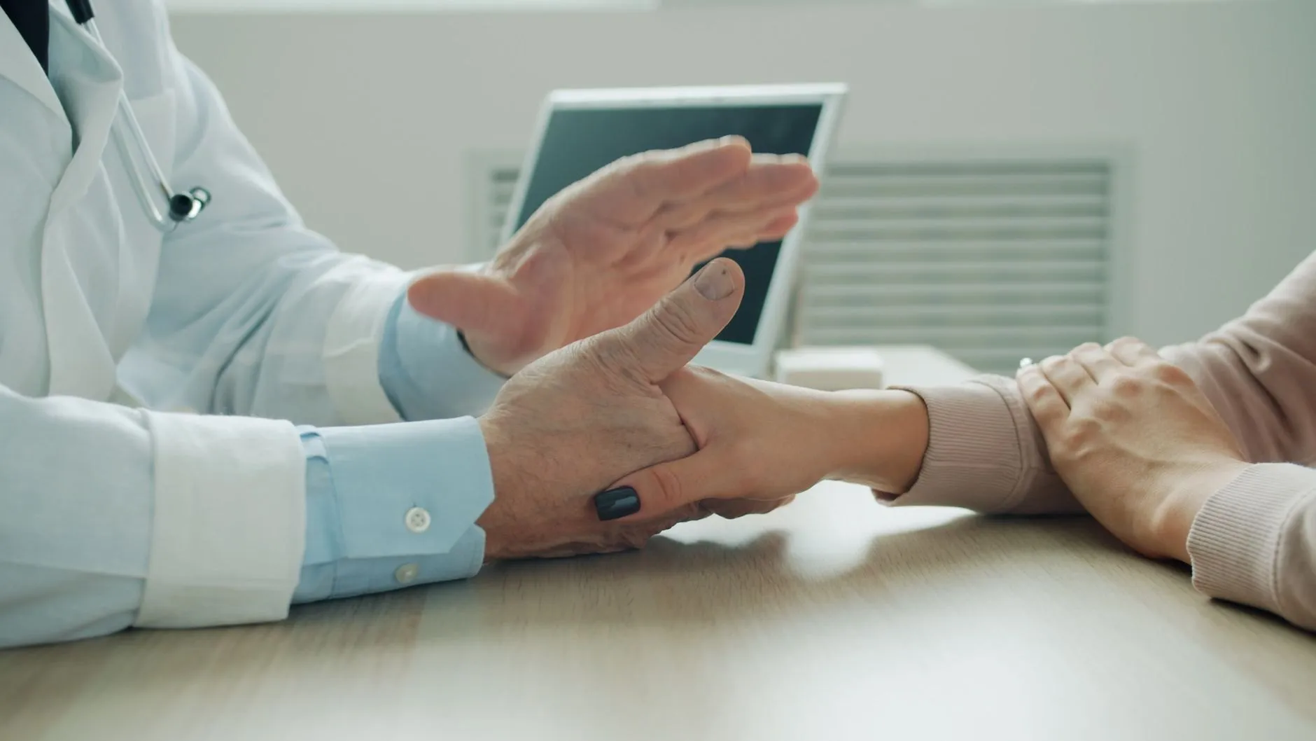An audiologist's hands over a patient's hands across a clinic desk during a consultation