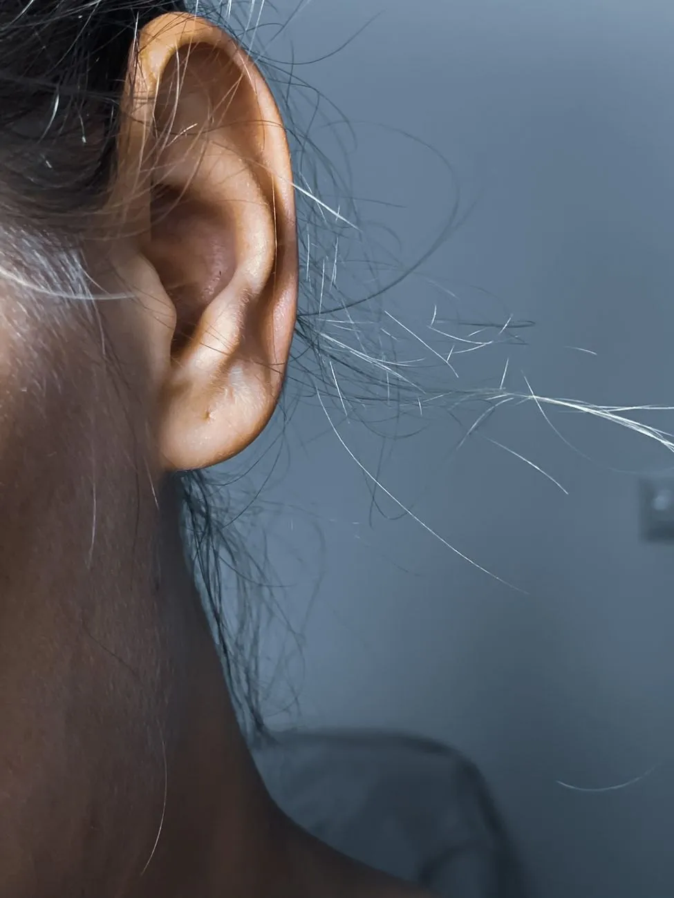 Close view of a woman's ear lit by soft window light, loose strands of hair catching the light