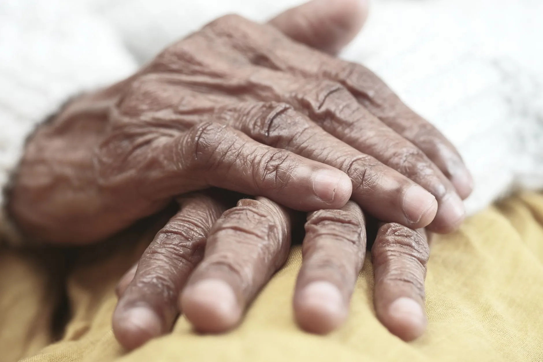 An older person's hands resting one over the other on a mustard-yellow blanket