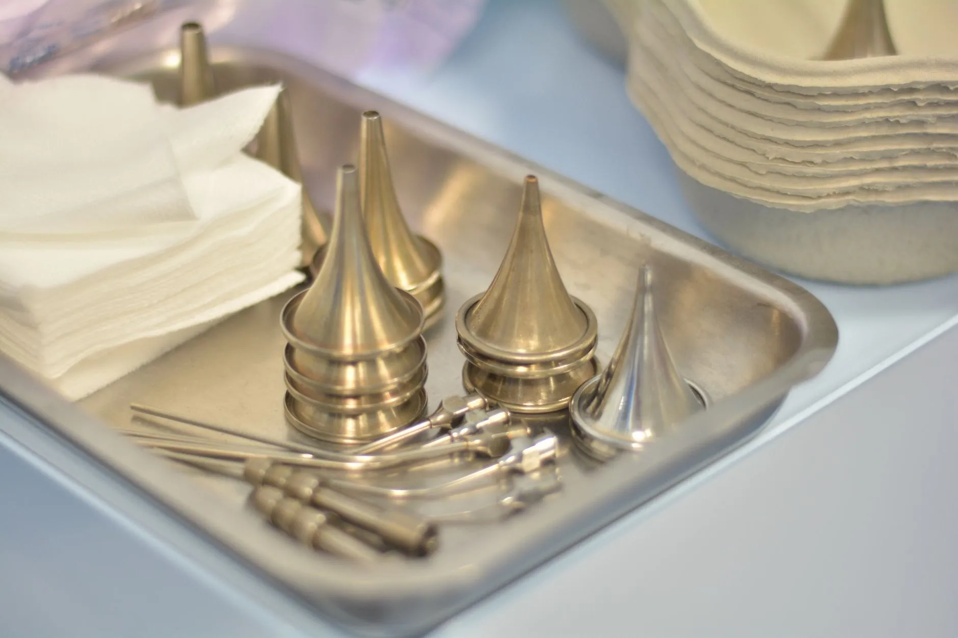 Steel ear specula and fine instruments laid out on a clinic tray beside folded gauze