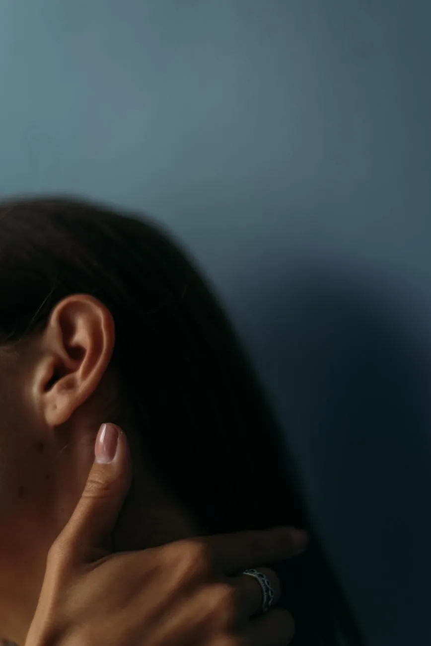 A woman's hand resting on her neck just below her ear, in soft blue-grey light