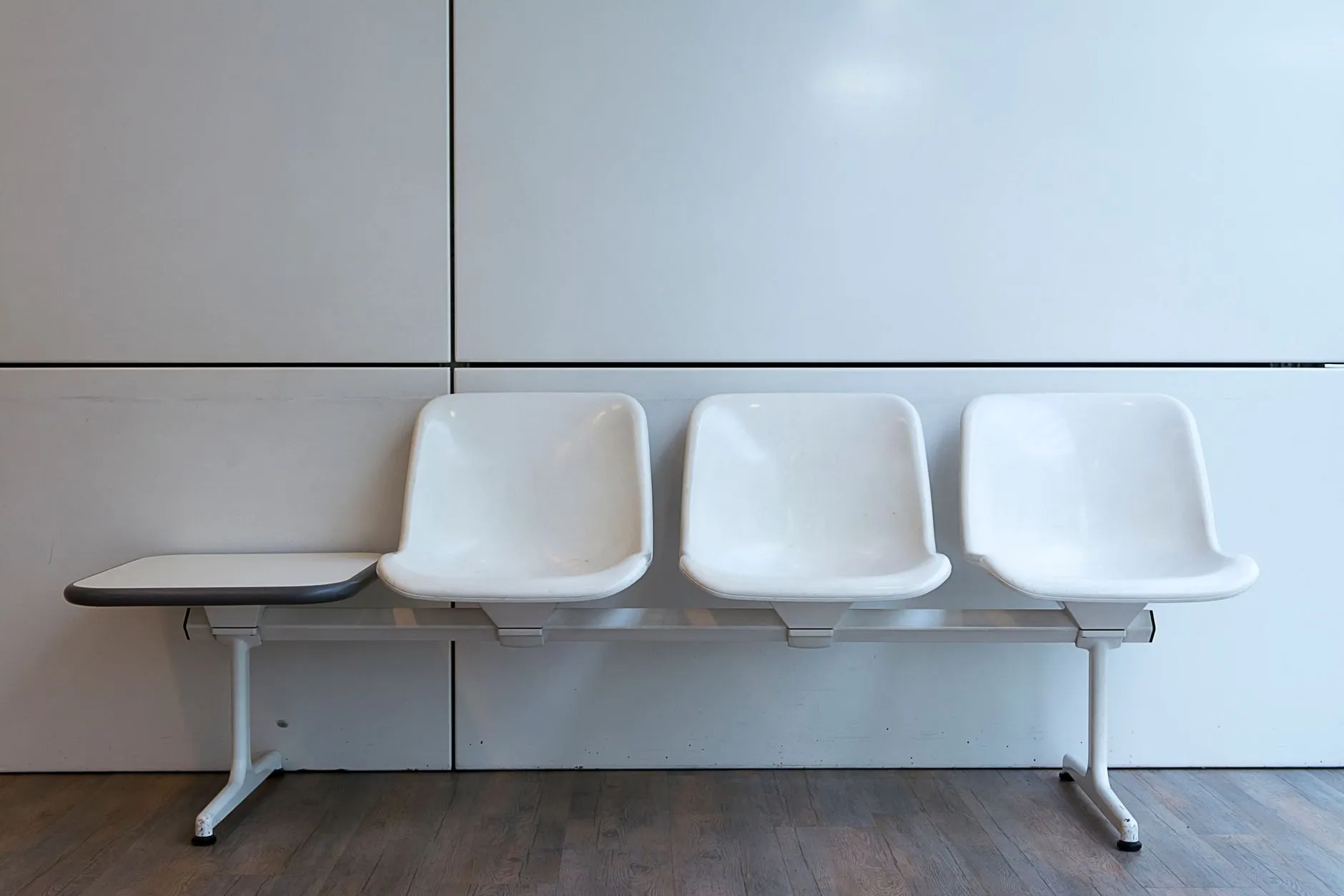A row of three white moulded waiting-room chairs with a small side table against a pale wall